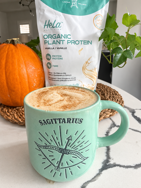 Warm pumpkin cinnamon smoothie in a mint mug next to a pumpkin and a bag of HeLa Organic Plant Protein in Vanilla